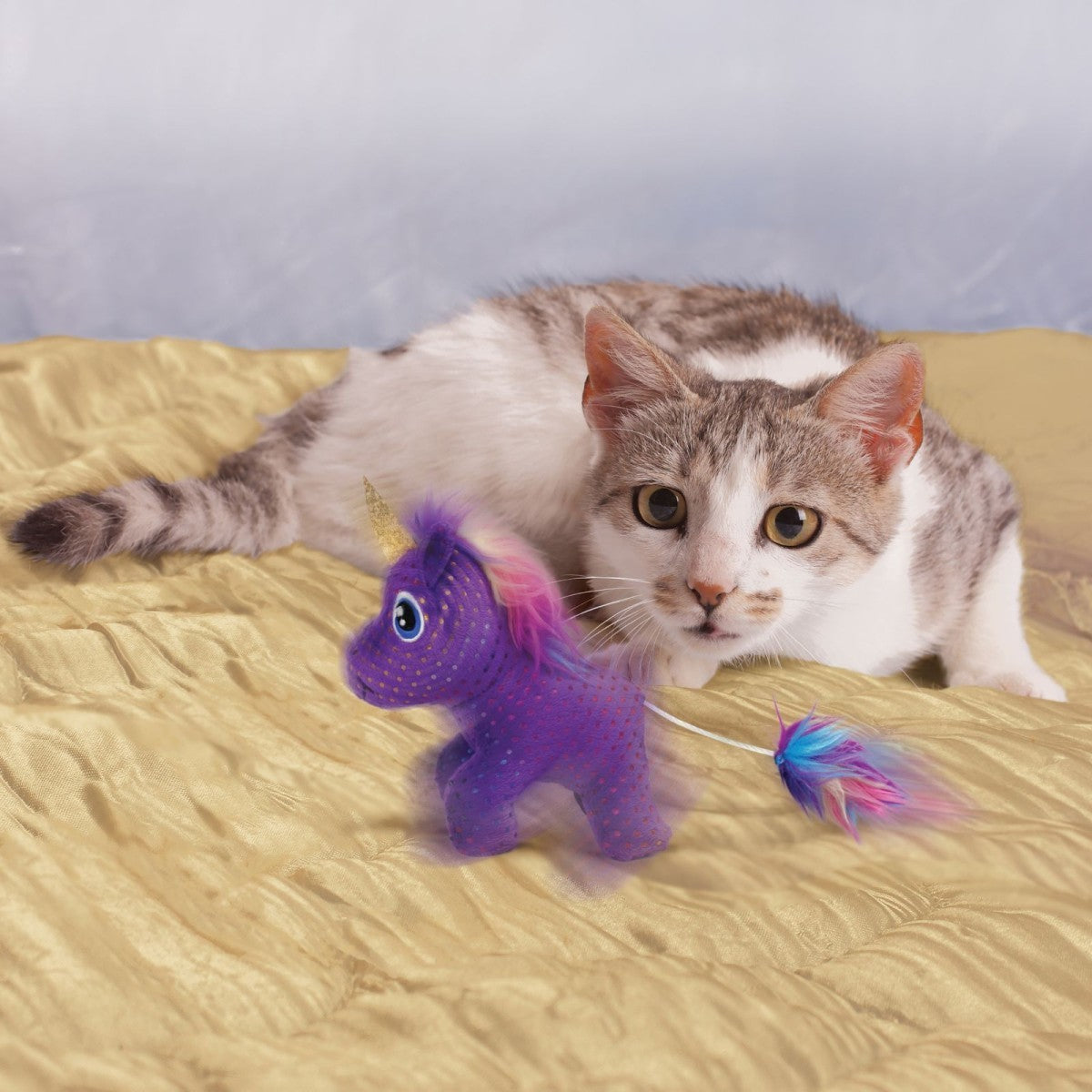 Cat playing with a purple unicorn toy on a bed